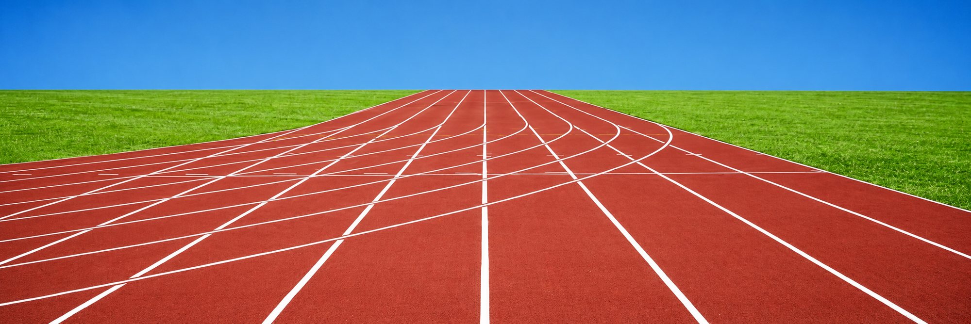 Vue en perspective d'une piste d'athlétisme rouge aux lignes blanches courbes, bordée de pelouse verte sous un ciel bleu.
